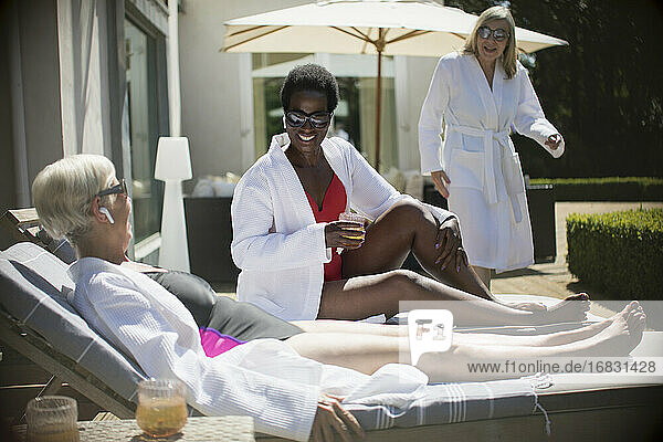 Happy senior women friends relaxing in spa robes on sunny hotel patio