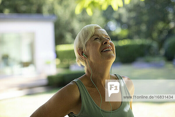Glückliche Seniorin mit Kopfhörern beim Training im Sommergarten