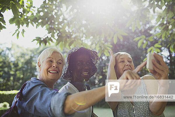 Playful senior women friends taking selfie in sunny summer garden