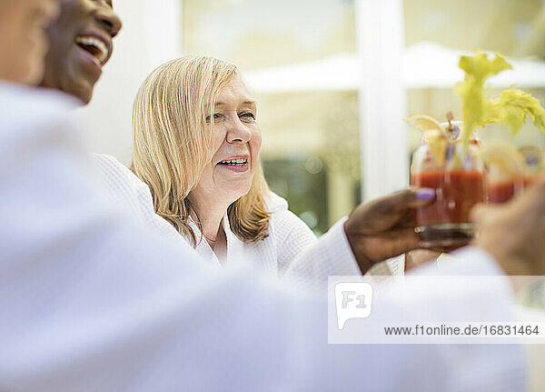 Glückliche Seniorin genießt Bloody-Mary-Cocktail mit Freunden