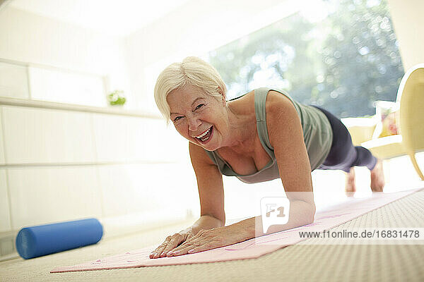 Porträt glücklich ältere Frau übt Planke Pose auf Yoga-Matte zu Hause