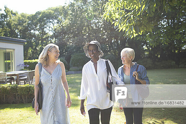 Happy senior women friends walking in sunny summer garden