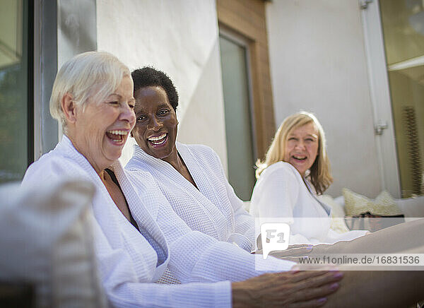 Happy women friends in spa bathrobes laughing on patio