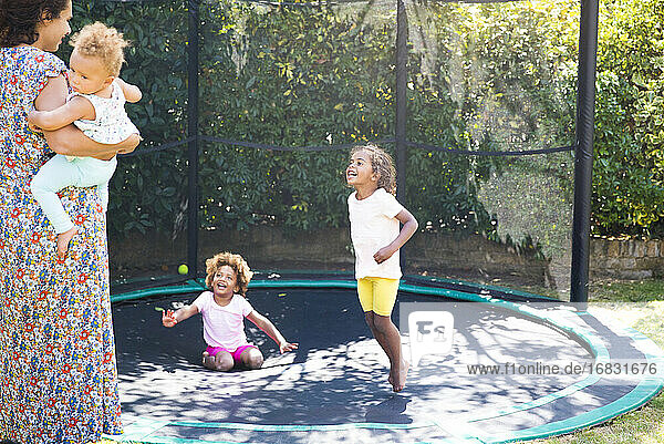 Glückliche Mutter und Töchter spielen auf sonnigen Hinterhof Trampolin
