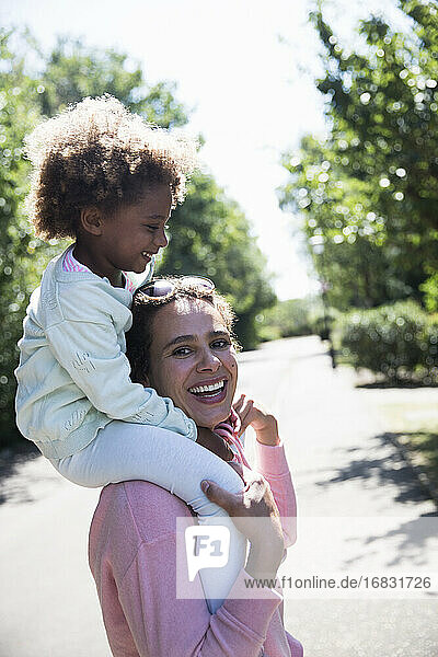 Porträt glückliche Mutter trägt Tochter auf den Schultern in sonnigen Straße