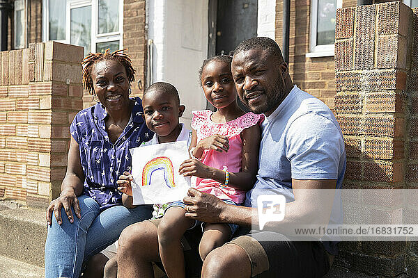 Portrait happy family with rainbow drawing on sunny front stoop