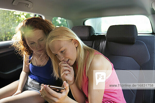 Preteen girl friends using smart phone in back seat of car