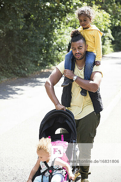 Vater trägt und schiebt Tochter im Kinderwagen auf sonnigen Weg