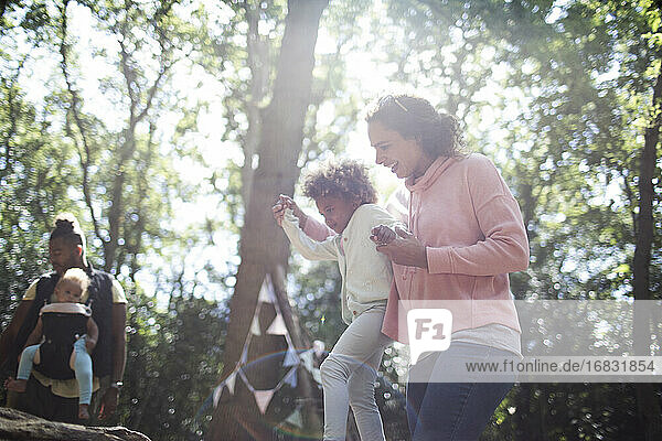 Mother helping daughter balance on fallen log in sunny woods