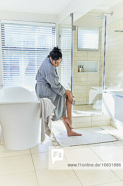 Frau im Bademantel berühren Bein im Haus Schaufenster Interieur Bad