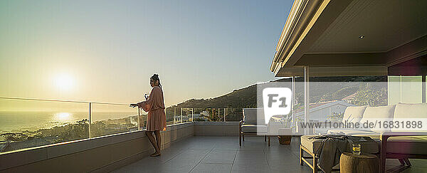 Frau mit Weißwein genießt Sonnenuntergang Meerblick auf Luxus-Balkon