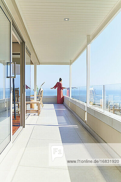 Frau im Kleid genießen sonnigen Blick auf das Meer von Luxus-Balkon