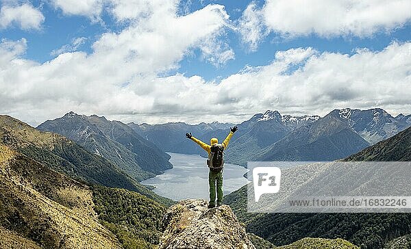 Mountaineer  hiker looks into the distance  stretching arms in the air  view of the South Fiord of Lake Te Anau  Murchison Mountains and Southern Alps in the background  on the Kepler Track hiking trail  Fiordland National Park  Southland  New Zealand  Oceania