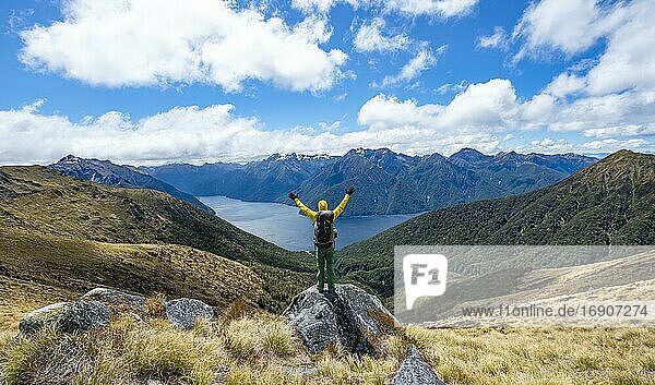 Hiker looks into the distance  stretches his arms in the air  view of the South Fiord of Lake Te Anau  Murchison Mountains in the background  on the Kepler Track  Great Walk  Fiordland National Park  Southland  New Zealand  Oceania