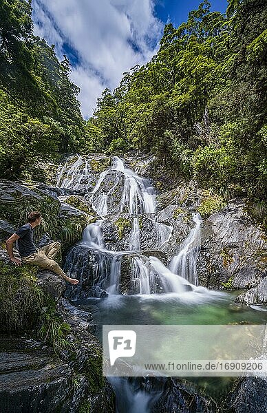 Junger Mann sitzt an einem Wasserfall  Fantail Falls  Makarora River  Wanaka  Westcoast  Südinsel  Neuseeland  Ozeanien