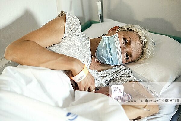 Mutter mit Atemschutzmaske stillt ihr neugeborenes Baby im Krankenhaus