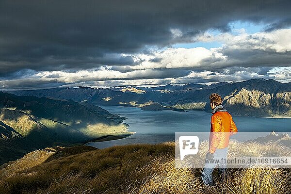 Hiker looks into the distance  view of Lake Hawea in the evening light  lake and mountain landscape  view from Isthmus Peak  Wanaka  Otago  South Island  New Zealand  Oceania