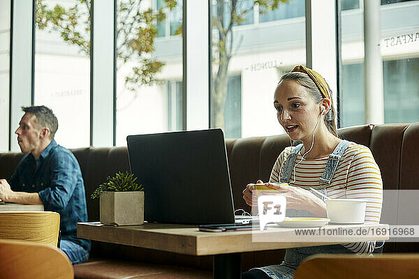 Frau  die in einem Café sitzt und einen Laptop benutzt und während eines Online-Anrufs interagiert