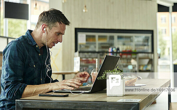 Mann in einem Café sitzend  an einem Laptop arbeitend