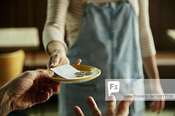 Frau hält einen Teller mit einer Cafe-Rechnung und Münzen heraus.