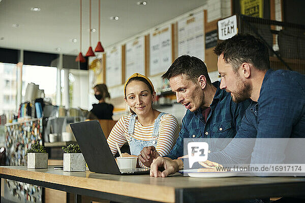 Two men and a woman seated in a cafe  looking at a laptop