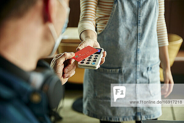 Frau hält kontaktloses Zahlungsterminal für einen Kunden  der mit Karte bezahlt