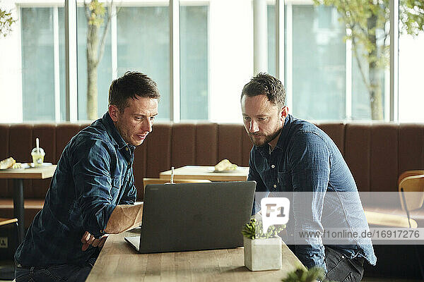 Zwei Männer  die in einem Café sitzen und auf einen Laptop-Bildschirm schauen