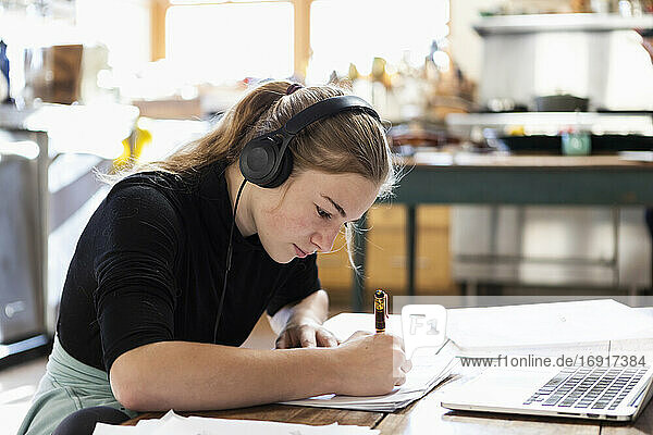 Teenager-Mädchen mit Kopfhörern  die einen Laptop benutzen und in ein Notizbuch schreiben