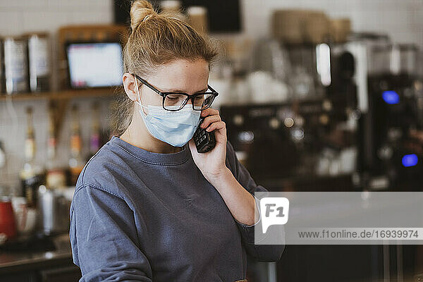 Kellnerin mit Gesichtsmaske bei der Arbeit in einem Café  am Telefon.