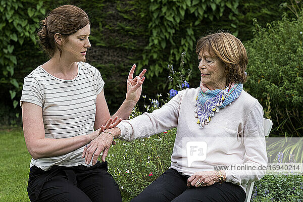 Frau und Therapeutin bei einer alternativen Therapiesitzung in einem Garten.