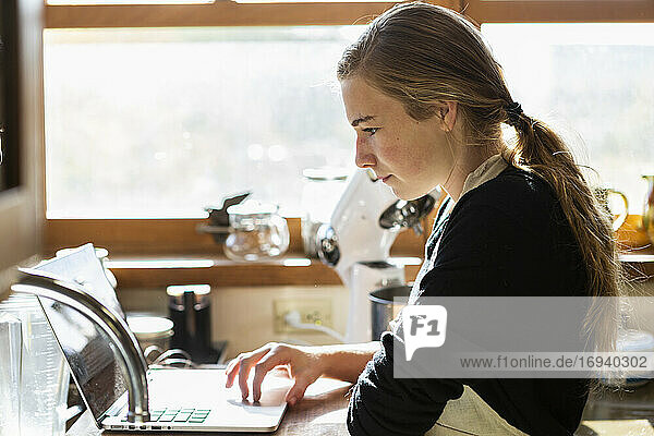 Teenager-Mädchen in einer Küche nach einem Backrezept auf einem Laptop.