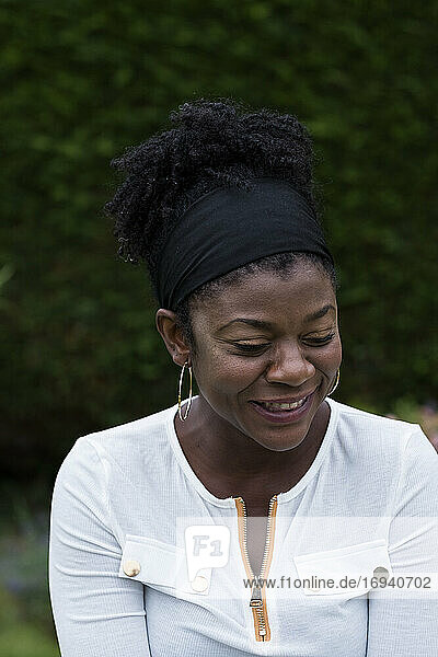 Porträt einer schwarzen Frau  die in einem Garten sitzt und während einer alternativen Therapiesitzung lächelt.
