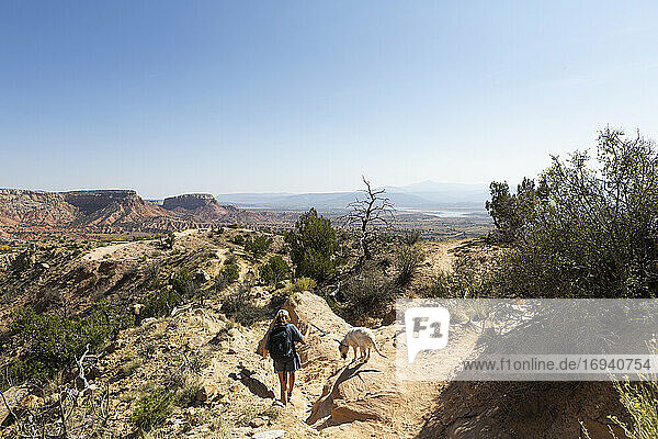 Teenager-Mädchen und ihr Retriever-Hund wandern auf einem Pfad durch eine geschützte Canyon-Landschaft
