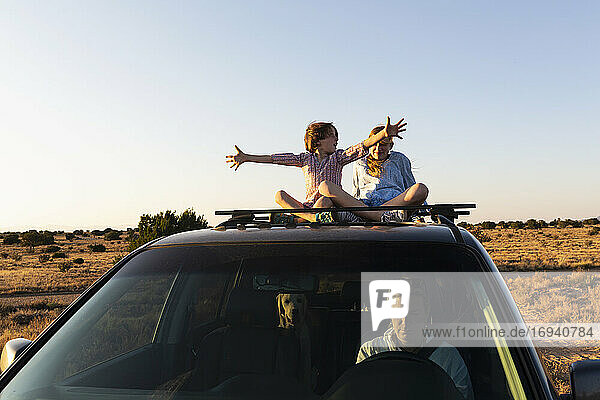 Teenage girl and her younger brother on top of SUV on desert road