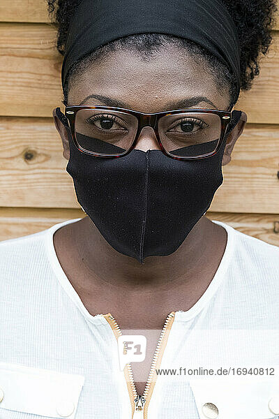 Porträt einer schwarzen Frau mit Brille und Gesichtsmaske  die in die Kamera schaut.