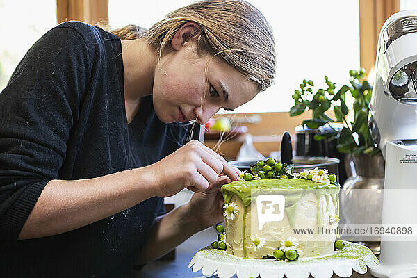 Teenage girl in kitchen applying icing to cake