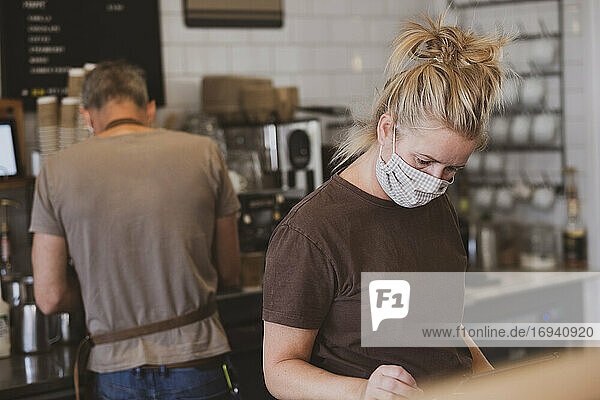 Kellnerin mit Gesichtsmaske bei der Arbeit in einem Cafe.