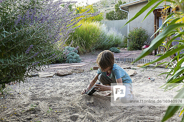 7 year old boy playing in sandy garden with his toy ship.