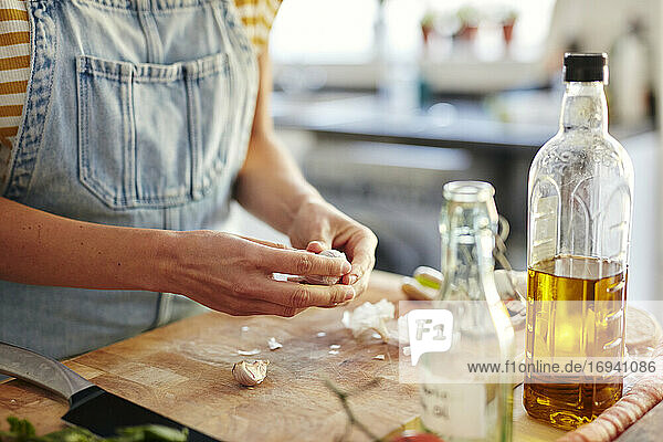 Woman in kitchen preparing garlic for cooking on chopping board