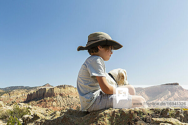 young boy sitting on rock with his dog