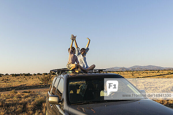 Teenage girl and her younger brother on top of SUV on desert road