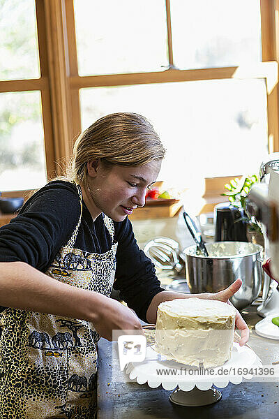 Teenage girl in kitchen applying icing to cake