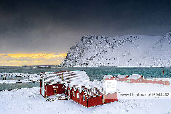 Wintersonnenuntergang über dem arktischen Meer und Fischerhütten im Schnee  Sorvaer  Insel Soroya  Hasvik  Troms og Finnmark  Norwegen  Skandinavien  Europa