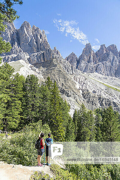 Rear view of two young hikers admiring the Odle from the famous Adolf Munkel trail  Val di Funes  South Tyrol  Dolomites  Italy  Europe