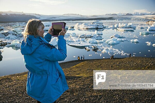Frau  die im Urlaub an der Jokulsarlon Gletscherlagune  einem mit Eisbergen gefüllten Gletschersee im Südosten Islands  ein Foto mit einem ipad macht