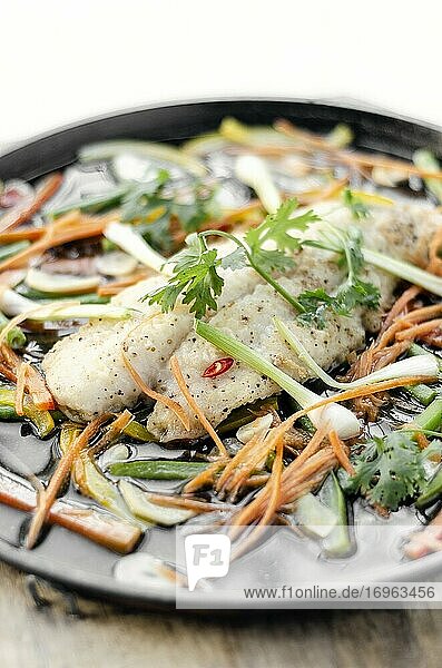 Gedämpftes würziges Fischfilet nach kantonesischer Art mit Gemüse auf einer heißen Platte.