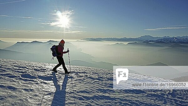 Wanderin beim Abstieg über Schneefeld vom Monte Lema  Nebel über dem Lago Maggiore. hinten Monte Rosa Massiv  Luino  Lombardei  Italien  Europa