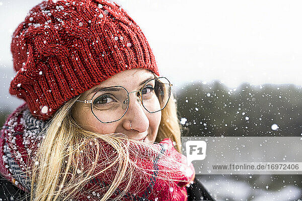 Smiling woman wearing wool bonnet and scarf in a winter cold day. Happy girl in a sweater outdoor in snow.