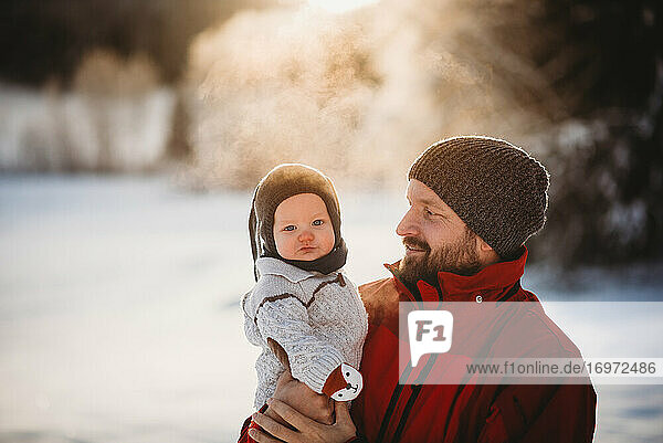 Papa und schöne Baby draußen im Schnee im Winter während goldenen Sonnenuntergang