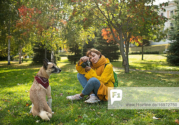 Freudige Frau  die ihren Hund im Park fotografiert